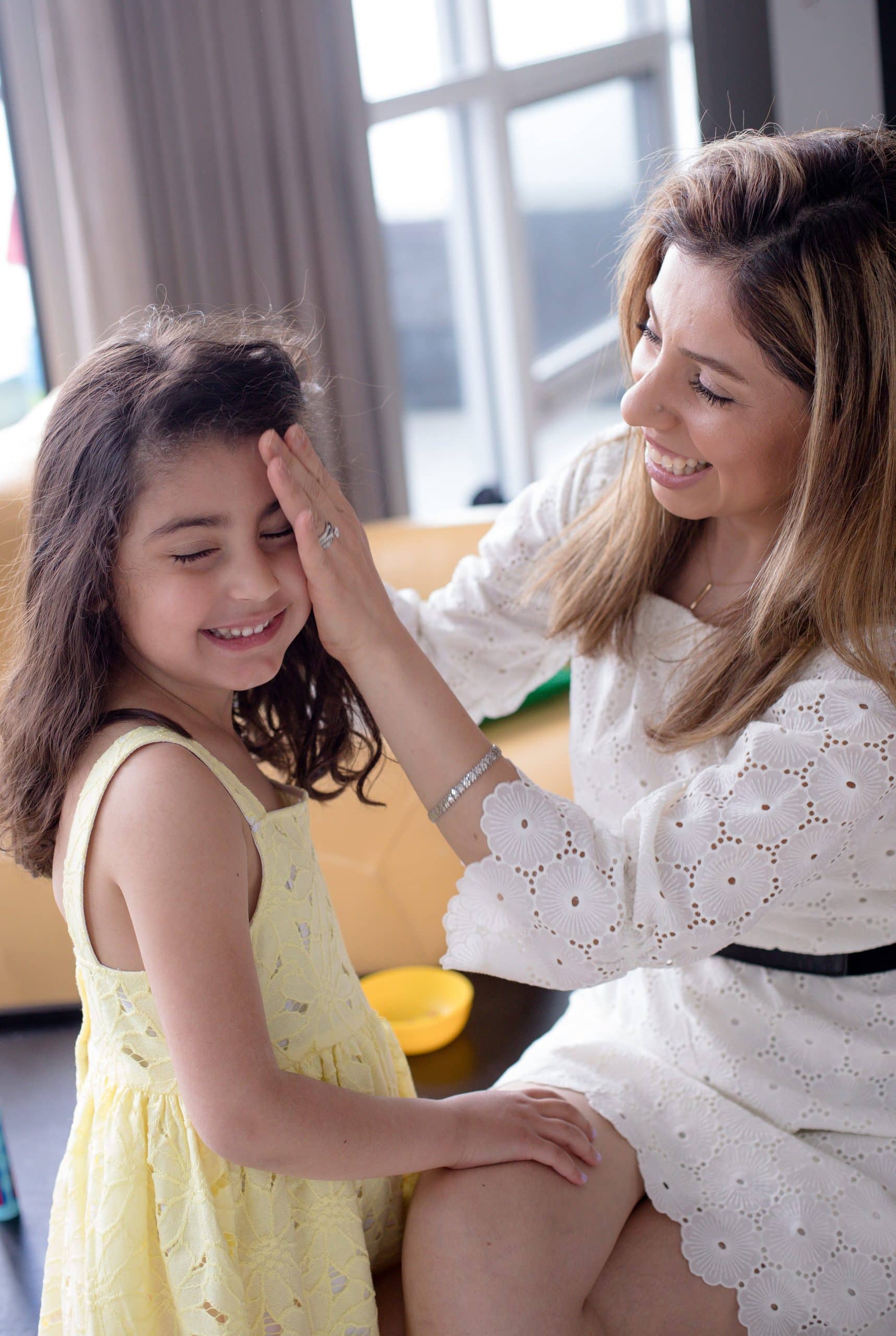 woman-sits-and-pulls-the-hair-back-from-a-childs-face A woman smiling as she reads a book with a young boy on the couch